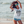 A woman posing on a beach wearing a white graphic t-shirt with black text, CATCH A WAVE, denim shorts, with ocean waves in the background.