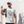 Man wearing a white t-shirt with text (styled in an eye-chart), Help, I need someone, standing against a light-colored wall.