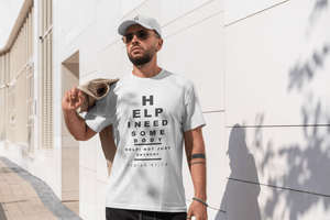 Man wearing a white t-shirt with text (styled in an eye-chart), Help, I need someone, standing against a light-colored wall.