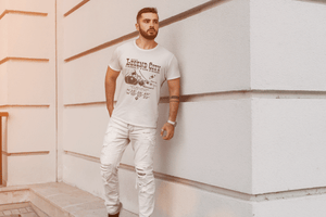 Man wearing a white t-shirt with text LEGEND CITY and graphics, with coordinates,standing against a textured wall.