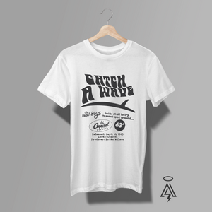A white short-sleeve graphic T-shirt. The shirt features a black vintage-style print with the text 'CATCH A WAVE', 'The Beach Boys', 'Capitol Records', and release details from September 16, 1963.
