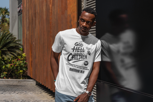 A man wearing a white graphic t-shirt with black text that reads 'GOD HELL IS NOT CHILDREN' and stands outdoors next to a corrugated metal wall.