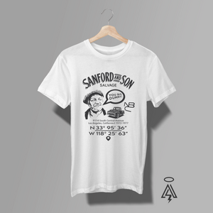A white short-sleeve graphic T-shirt. The shirt features a black vintage-style print with the text 'SANFORD AND SON SALVAGE', a caricature portrait of Fred Sanford with voice bubble "YOU BIG DUMMY!", a vintage truck, NBC logo and coordinates below it.