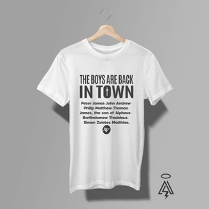 A white short-sleeve graphic T-shirt. The shirt features white text reading 'THE BOYS ARE BACK IN TOWN' followed by a list of the Disciples.