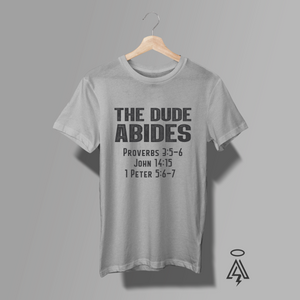 This heather gray tee "THE DUDE ABIDES" with a lineup of scripture references — Proverbs 3:5–6 • John 14:15 • 1 Peter 5:6–7.