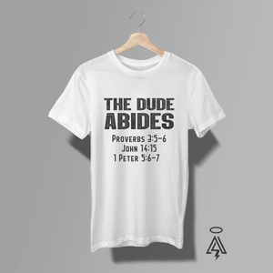 This white tee "THE DUDE ABIDES" with a lineup of scripture references — Proverbs 3:5–6 • John 14:15 • 1 Peter 5:6–7.